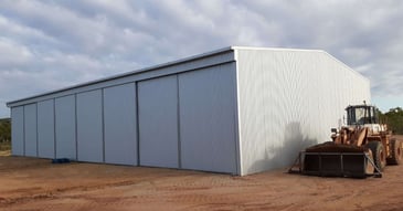 Durable hay shed design with steel gable roof and sliding doors, front-end loader beside it