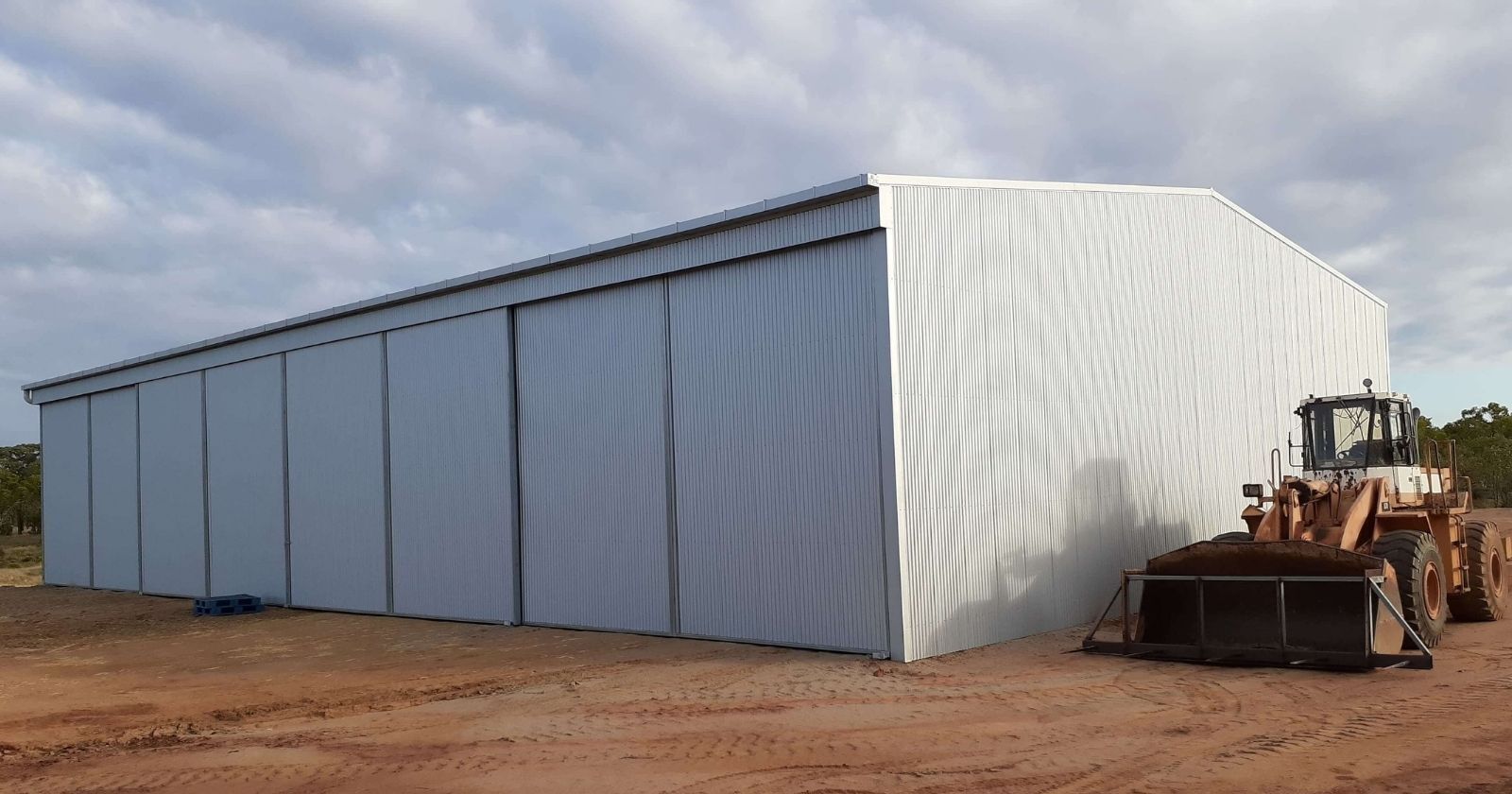 Durable hay shed design with steel gable roof and sliding doors, front-end loader beside it